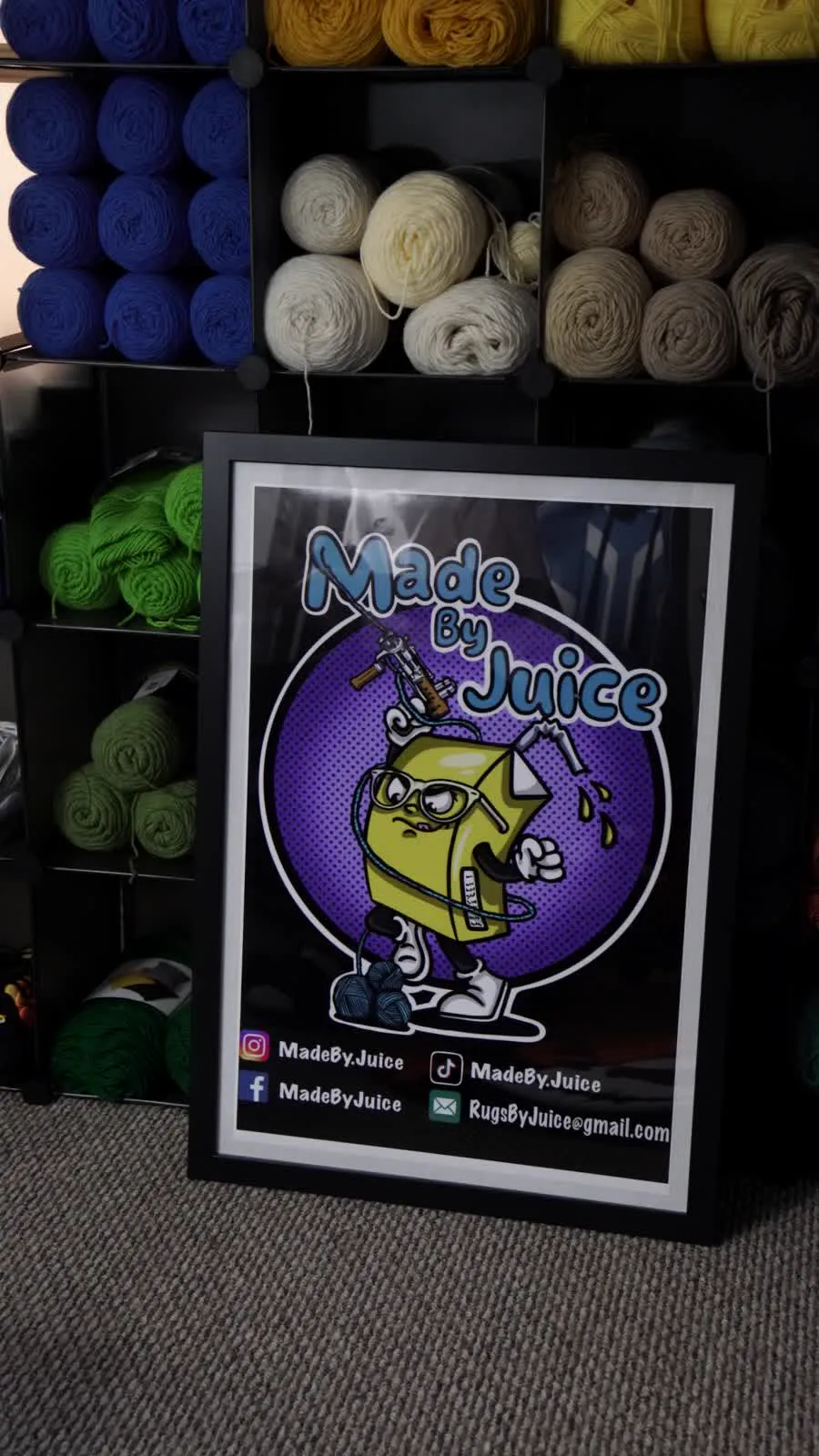 The framed Made By Juice poster leaning against cubbies of yarn in the studio